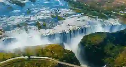 Aerial view of Victoria Falls in Zimbabwe, with water cascading over the cliffs and mist rising above the surrounding landscape