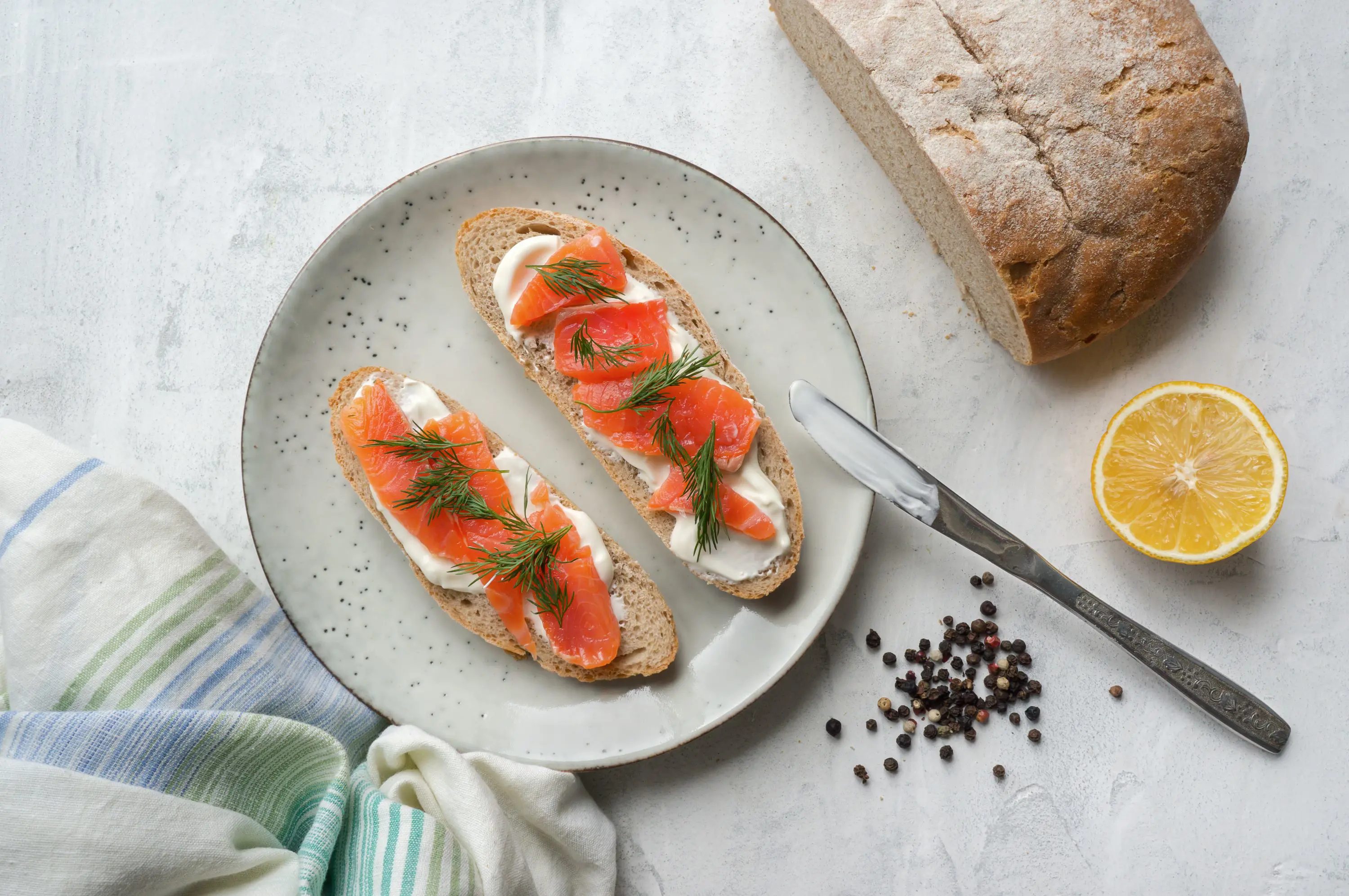 Gravalax on toast with cream cheese and dill, and a loaf of bread and lemon next to the plate