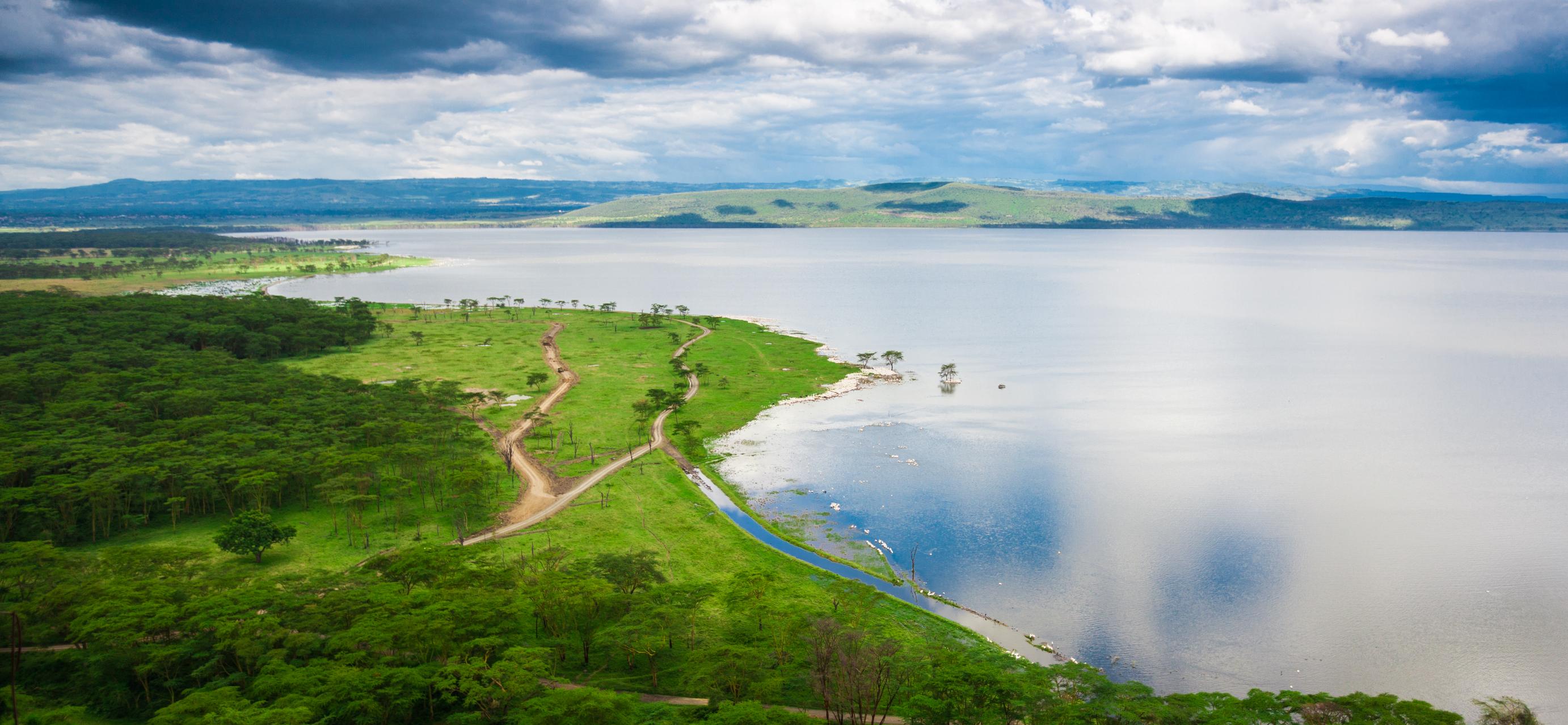 An aerial view of Lake Nakuru with green shores and cloudy skies
