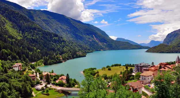 Molveno Lake in Italy, with colourful houses in the foreground and rolling hills alongside the lake