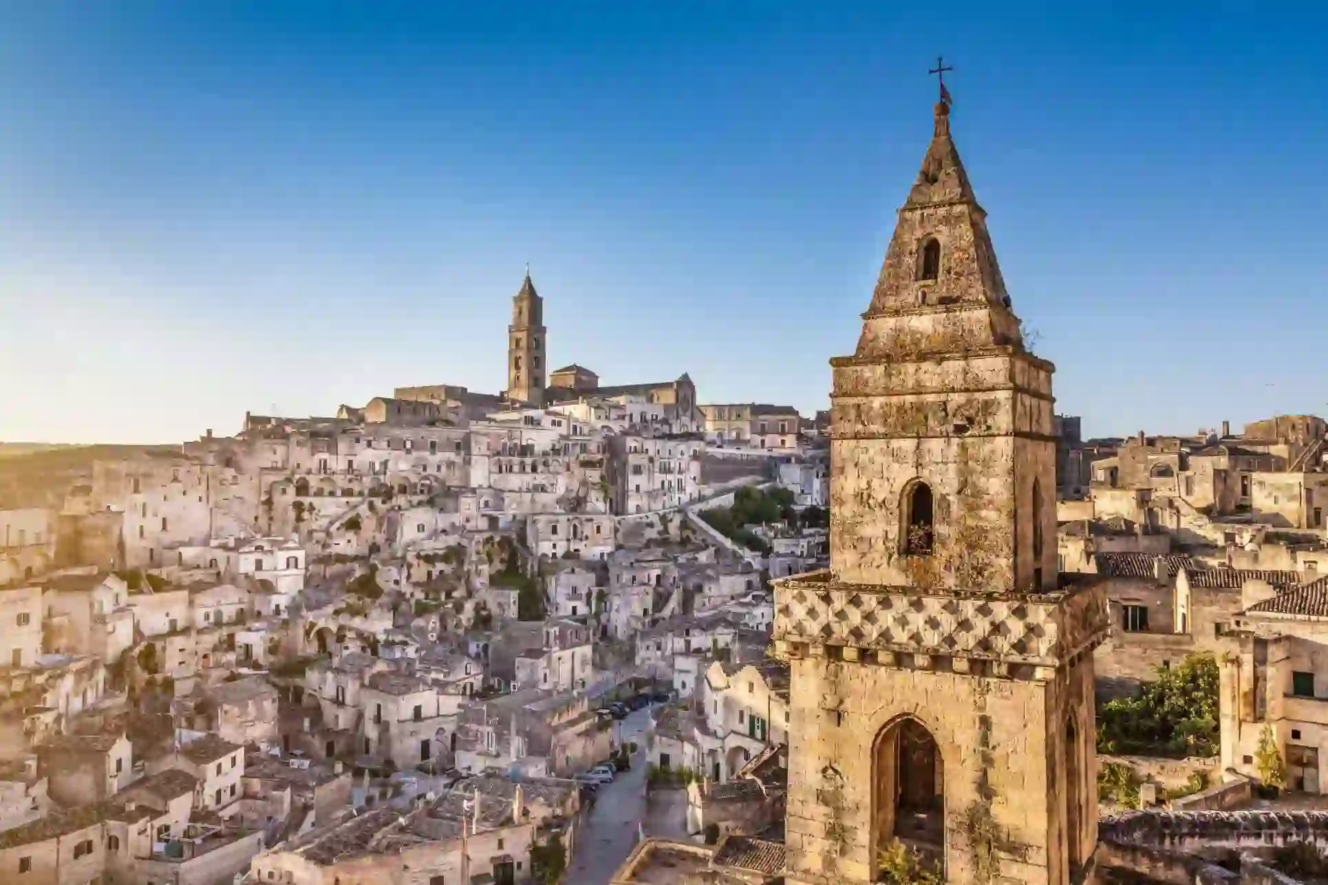 View of Matera’s ancient stone dwellings and rock-cut churches, with a bell tower overlooking the historic Sassi district under a clear blue sky
