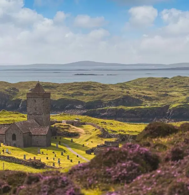 Long shot of St Clement's Church, showing the gravestones dotted around it, the hilly landscape and Loch Rodel in the distance 