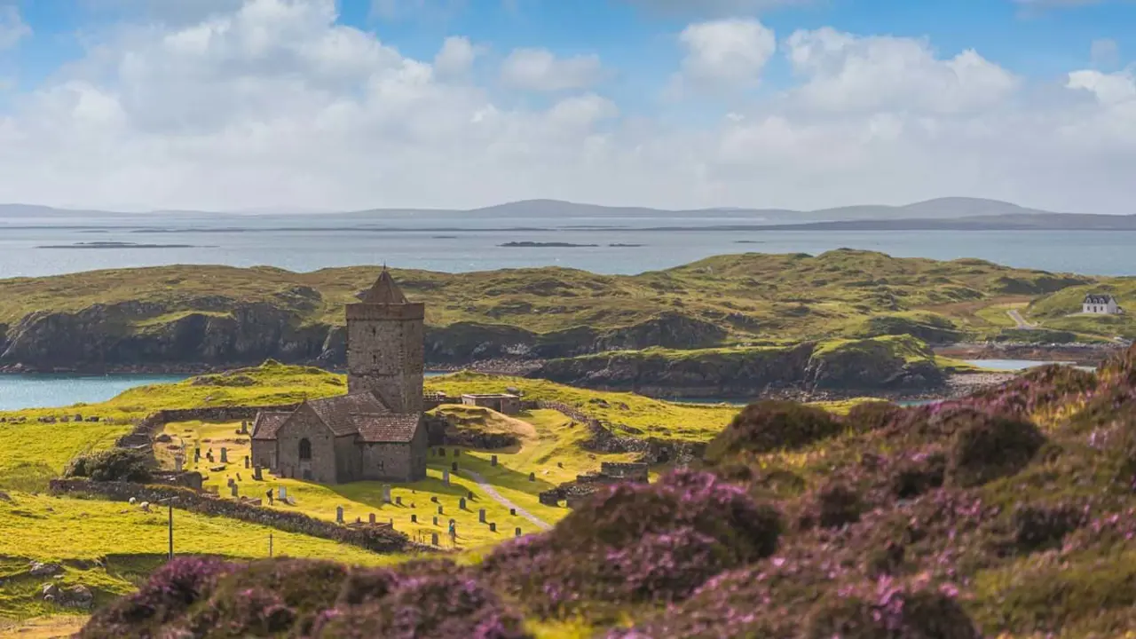 Long shot of St Clement's Church, showing the gravestones dotted around it, the hilly landscape and Loch Rodel in the distance 