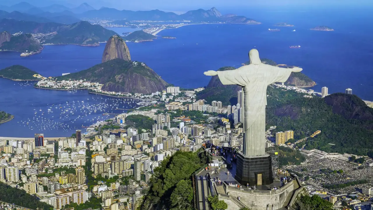Panoramic view of Rio de Janeiro with Sugarloaf Mountain, the Christ the Redeemer statue, and city buildings along the coastline
