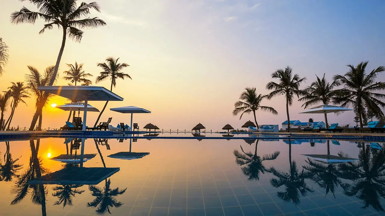 Exterior pool at ITC Hotels in Mahabalipuram at sunset, with silhouetted palm trees reflected in the water