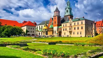 Wawel Castle in Kraków, Poland, showcasing its historic towers and red-brick walls beneath a cloudy blue sky