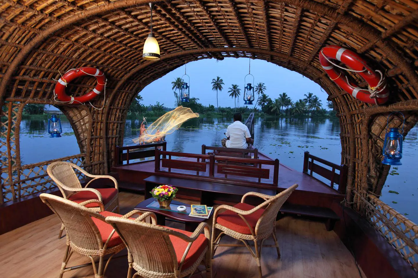 View from the lounge area of a Kerala houseboat sailing on the river, showing calm waters, lush greenery, and palm trees along the banks