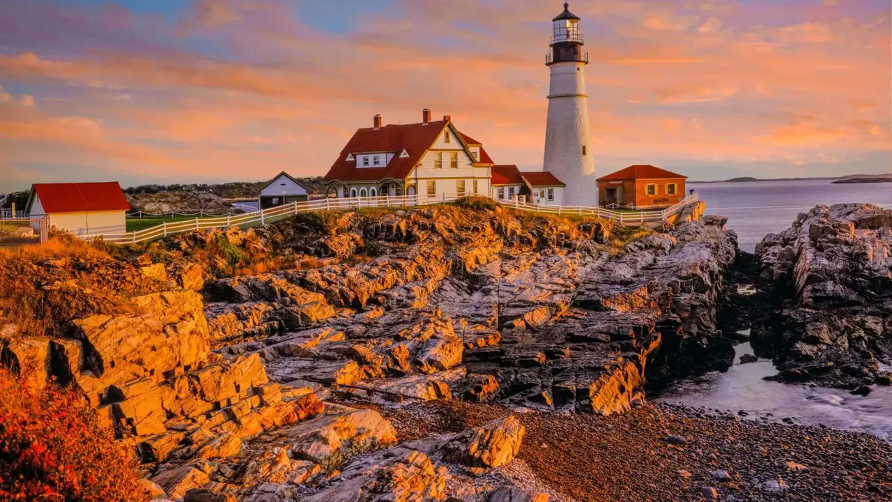 Portland Head Lighthouse on the rocky Maine coast at sunset, with warm colours in the sky reflecting over the Atlantic Ocean