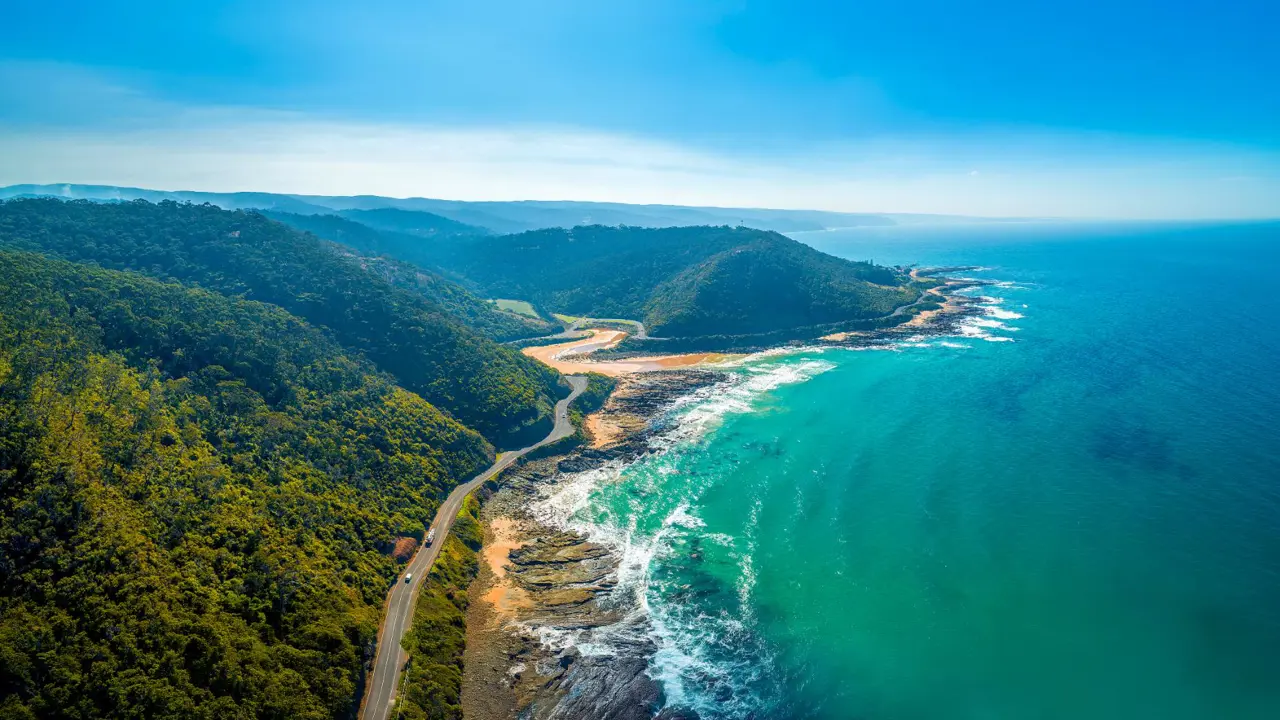 A winding section of the Great Ocean Road in Victoria, Australia, with turquoise waters and rugged cliffs.