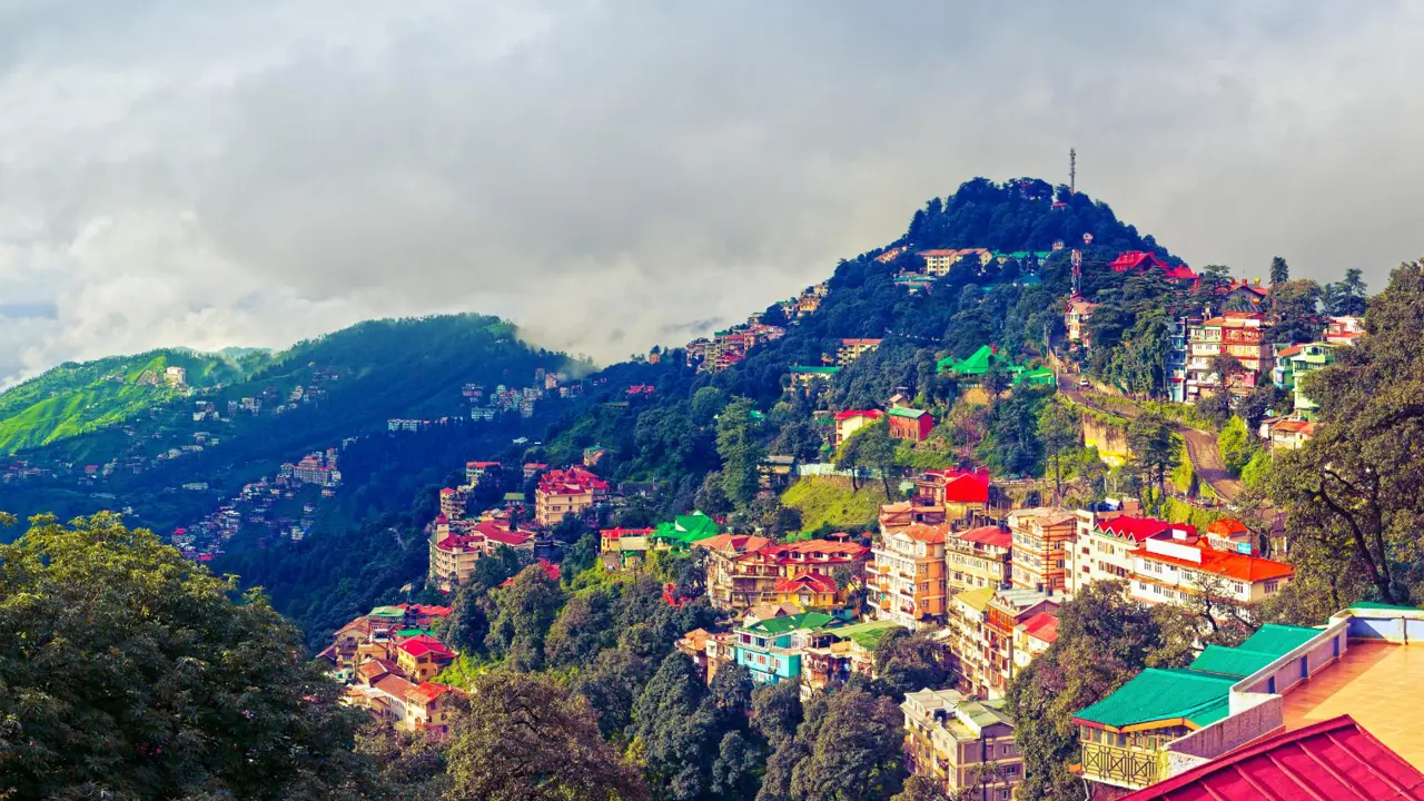 A panoramic view of Shimla’s colourful hillside buildings surrounded by green mountains and misty clouds in the Himalayan foothills