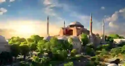 Hagia Sophia with its domes and minarets at sunset, surrounded by green trees in Istanbul