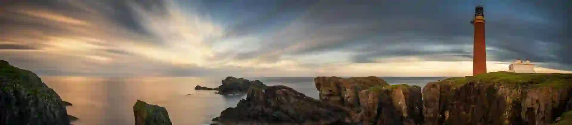 Long shot of the coast of the Isle of Lewis at sunset, showing the Butt of Lewis Lighthouse on the far right, looking out to sea