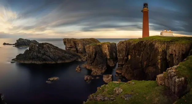 Long shot of the coast of the Isle of Lewis at sunset, showing the Butt of Lewis Lighthouse on the far right, looking out to sea