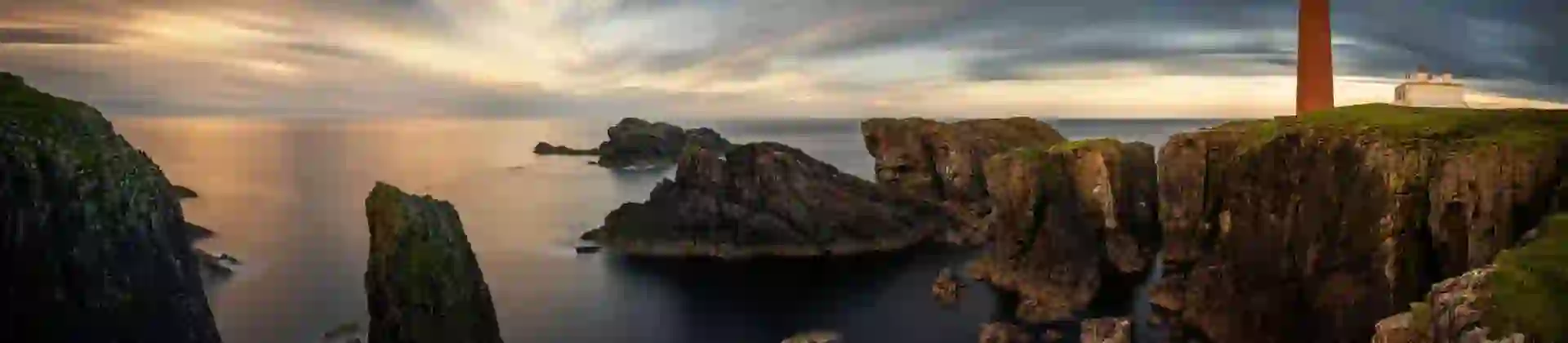 Long shot of the coast of the Isle of Lewis at sunset, showing the Butt of Lewis Lighthouse on the far right, looking out to sea