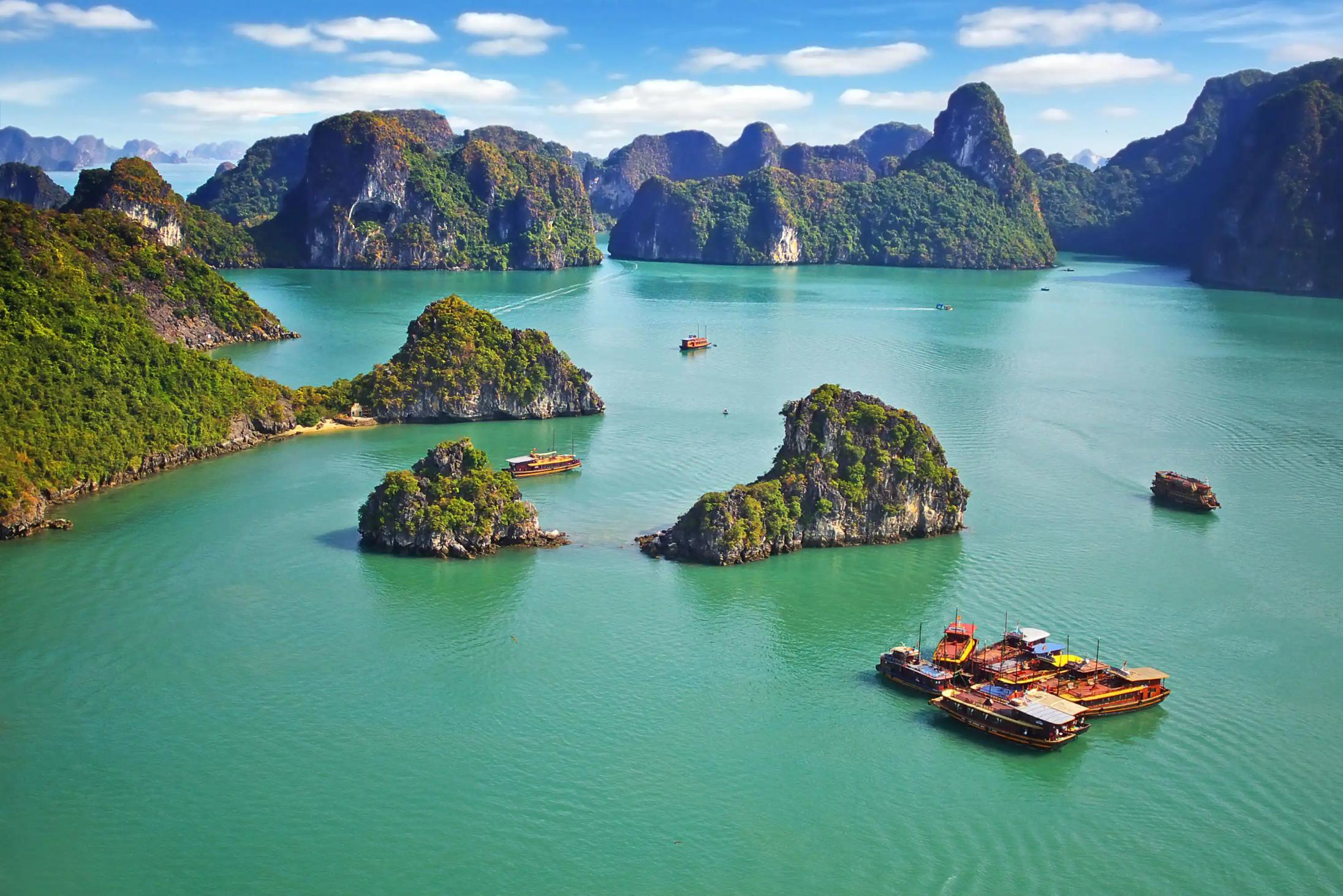 Traditional wooden boats sailing among limestone islands in Ha Long Bay, Vietnam