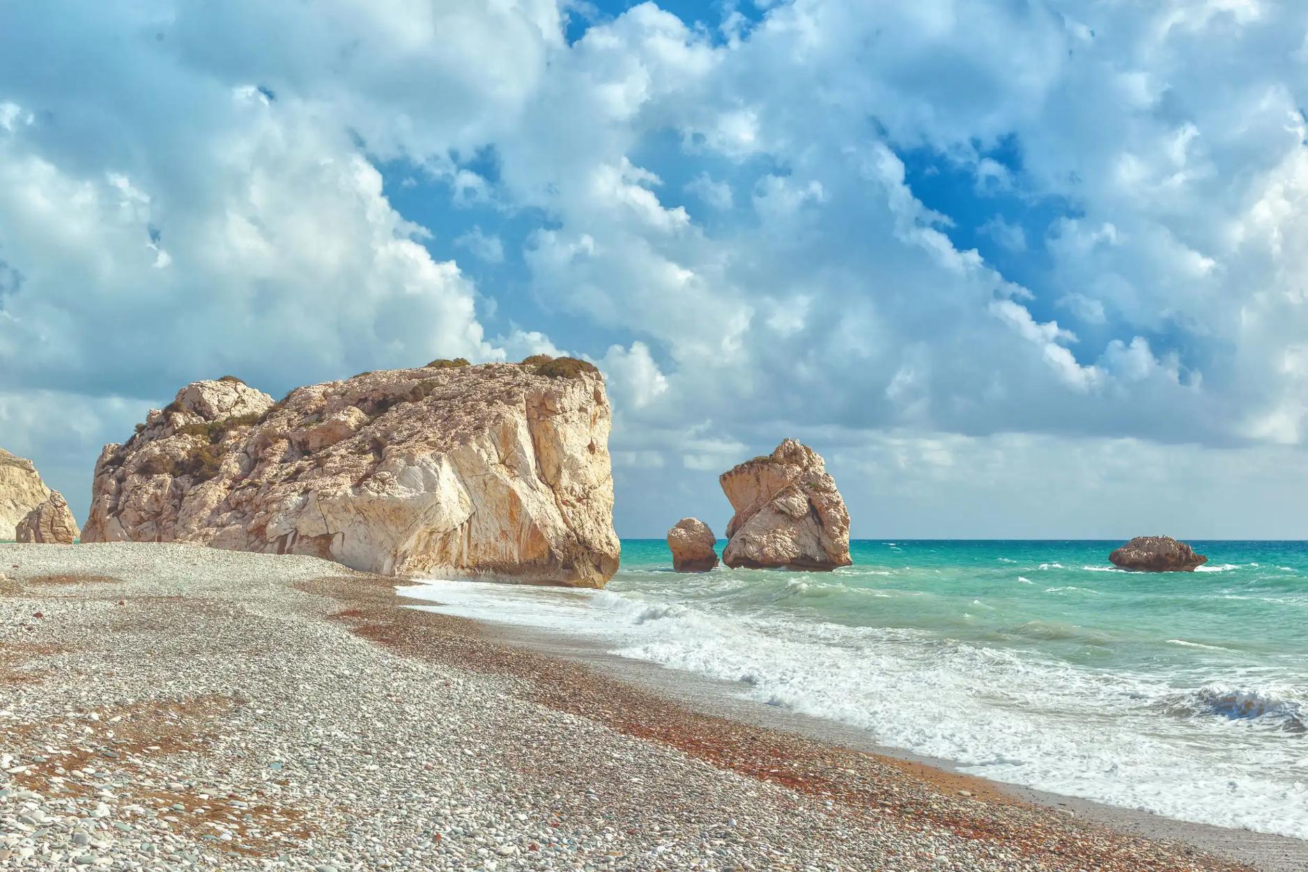 A cloudy day with waves crashing on a pebbled beach near Aphrodite’s Rock in Cyprus
