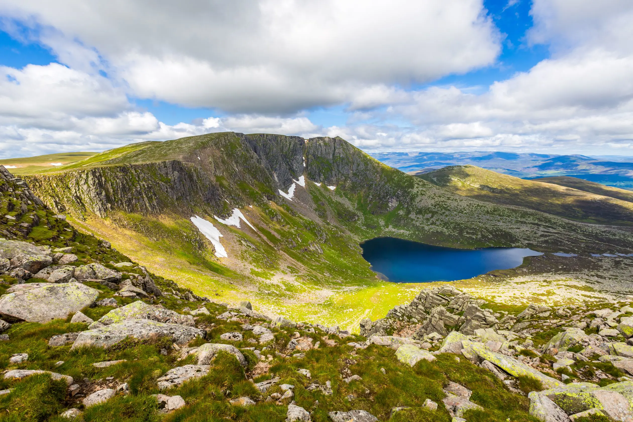 View of Cairngorms National Park, with a small body of water in the centre and a cloudy, but blue sky