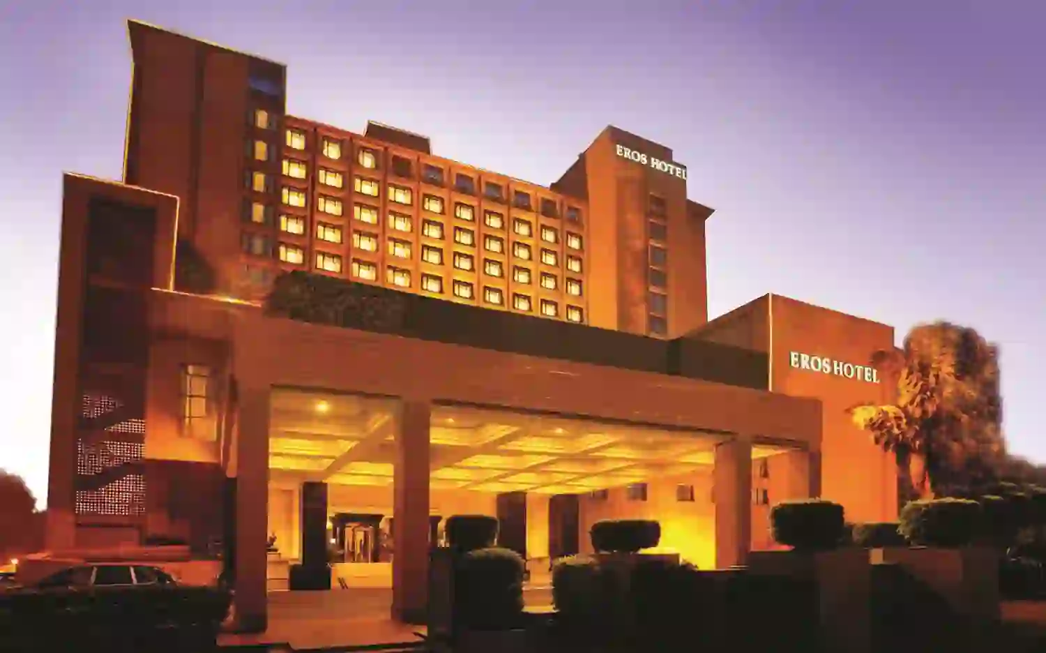 Exterior of the Eros Hotel in New Delhi at dusk, with golden lighting highlighting the grand entrance and tall façade