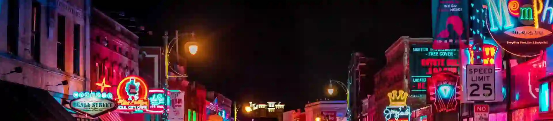 Vibrant night scene on Beale Street in Memphis, with neon signs glowing above blues clubs, bars, and live music venues, and crowds of people walking along the historic street