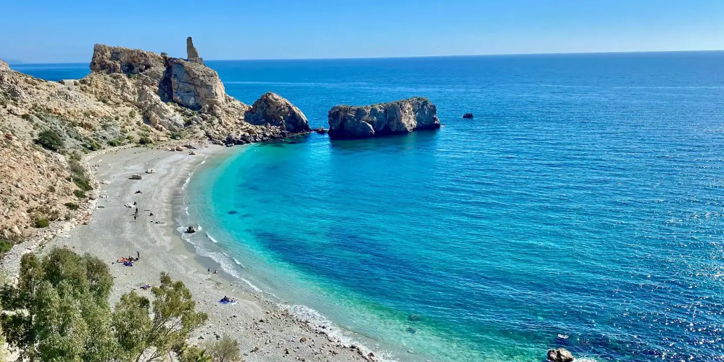 A wide sandy beach along the Costa de la Luz in Andalucía, Spain, with gentle waves lapping the shore under a clear blue sky