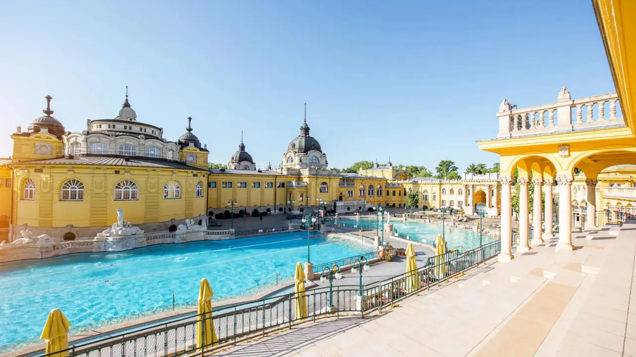 Two outdoor pools surrounded by grand yellow neo-baroque buildings on a sunny day at Széchenyi Thermal Baths in Budapest