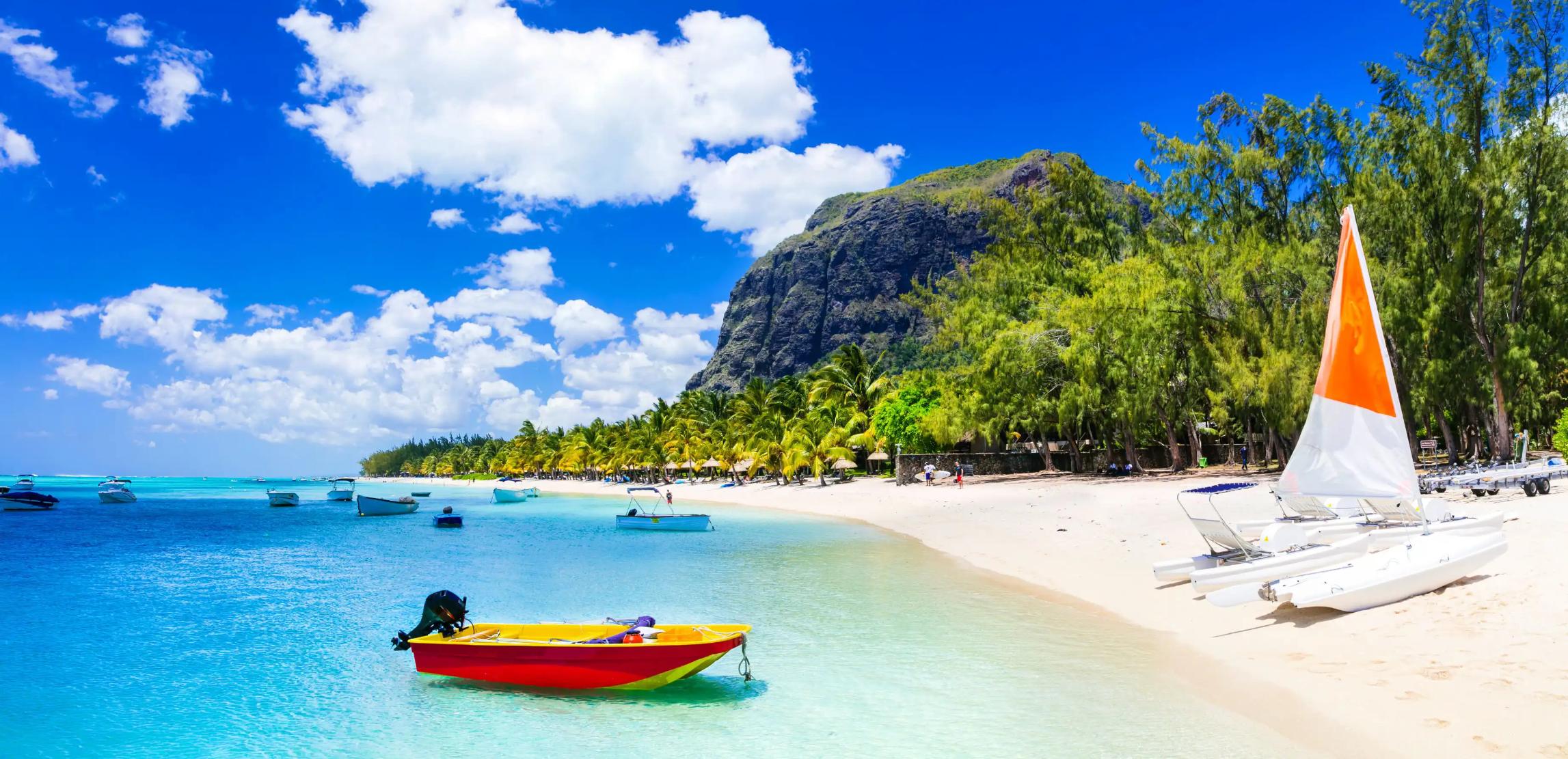View of Mauritius featuring clear blue water, several boats floating on the sea, and a yacht on the sandy shore