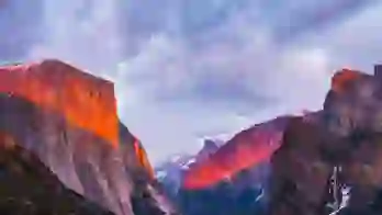 A dramatic view of Yosemite’s El Capitan and surrounding mountains bathed in warm, glowing sunset light under a cloudy sky
