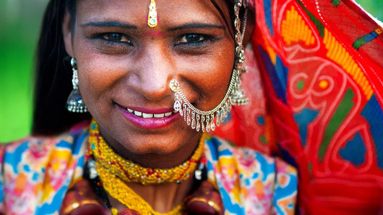 A close-up of a smiling Rajasthani woman dressed in vibrant traditional clothes and jewellery in Rajasthan in India