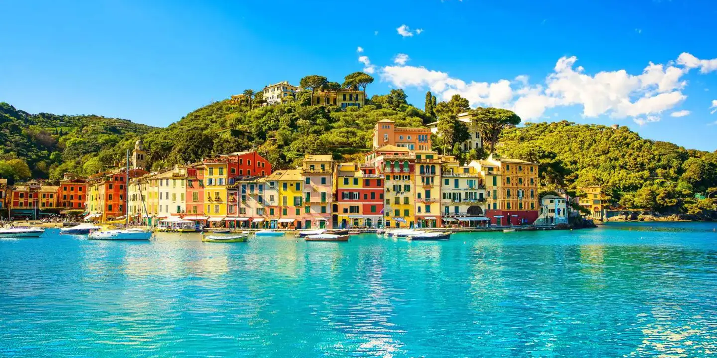 Picturesque view of Portofino, Italy, featuring colourful harbourfront buildings, boats gently floating in the clear blue water, and lush green hills in the background