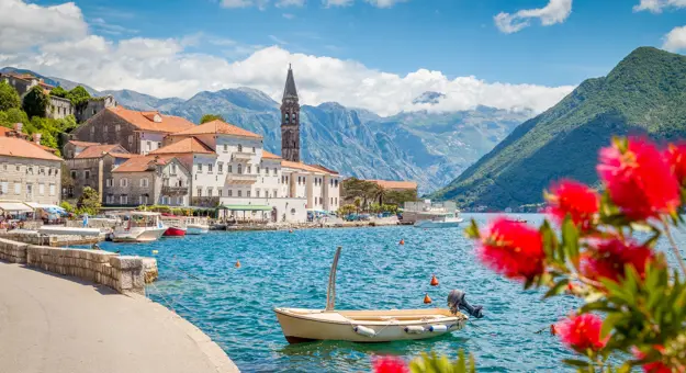 Scenic panorama view of the historic town of Perast at famous Bay of Kotor with blooming flowers on a beautiful sunny day with blue sky and clouds in summer, Montenegro, southern Europe