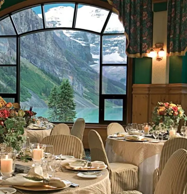 The elegant dining room at Fairmont Chateau with a view of Lake Louise and the Rocky Mountains through the arch windows