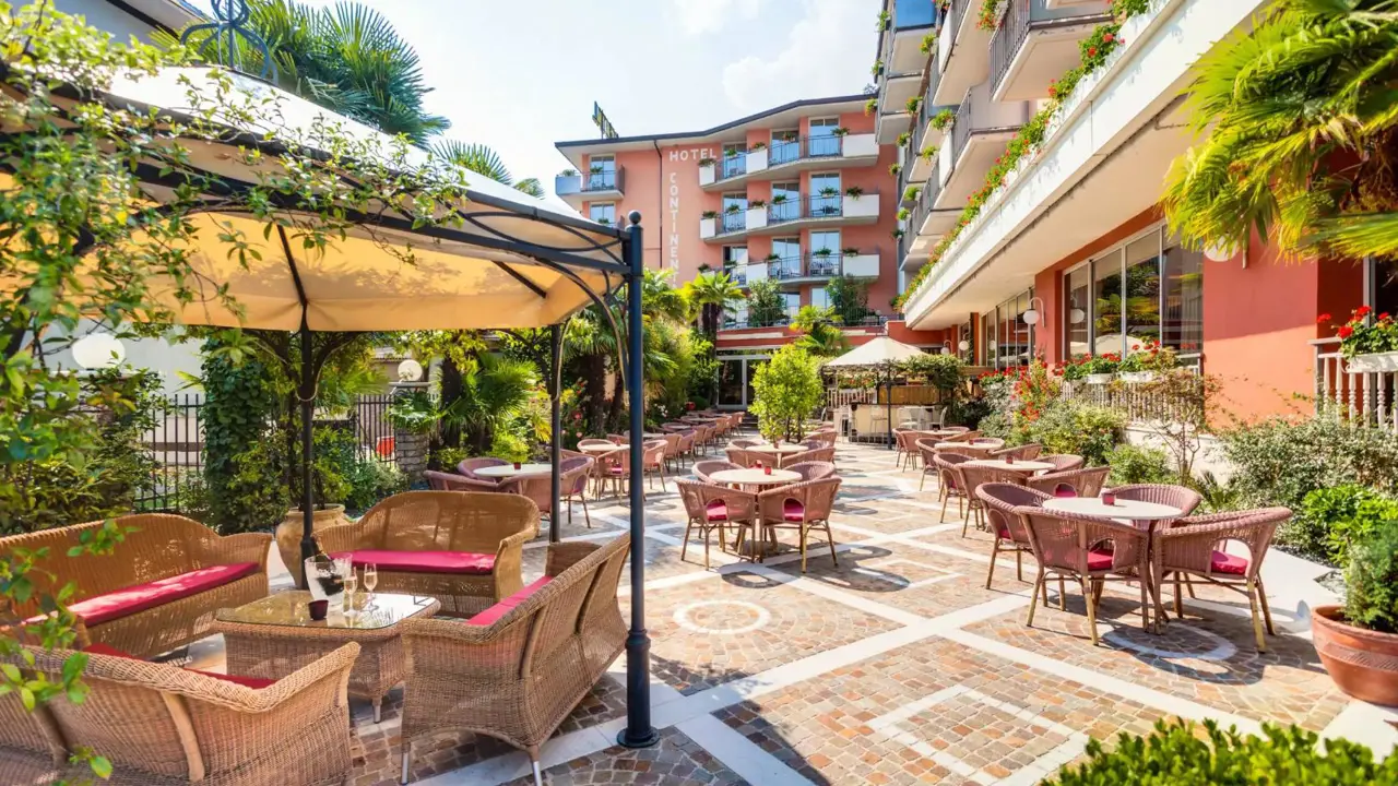 Sunny exterior dining area at Hotel Continental in Torbole, with wooden tables and chairs arranged for guests