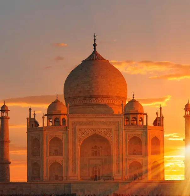 The Taj Mahal bathed in golden sunlight at sunset, with the sun setting between its elegant minarets, highlighting the detailed marble carvings and domed architecture