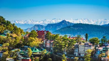 A panoramic view of Shimla, in the foothills of the Himalayas, with colourful hillside houses and pine forests set against the backdrop of snow-capped mountain peaks
