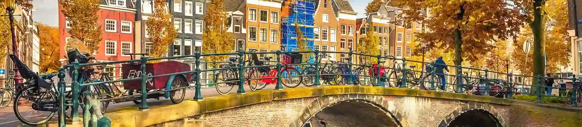A bridge in Amsterdam with bikes chained to the railing & houses in the background