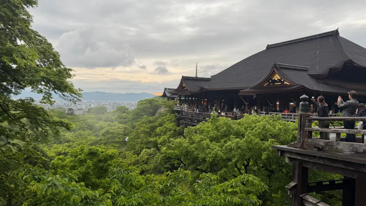 Kiyomizu-dera Temple in Kyoto, Japan, perched on a hillside with its large wooden terrace overlooking a forest of green trees