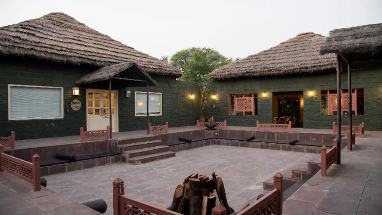 Traditional courtyard at Vannashyra Cottages with stone flooring, thatched-roof buildings, central fire pit, and cushioned seating