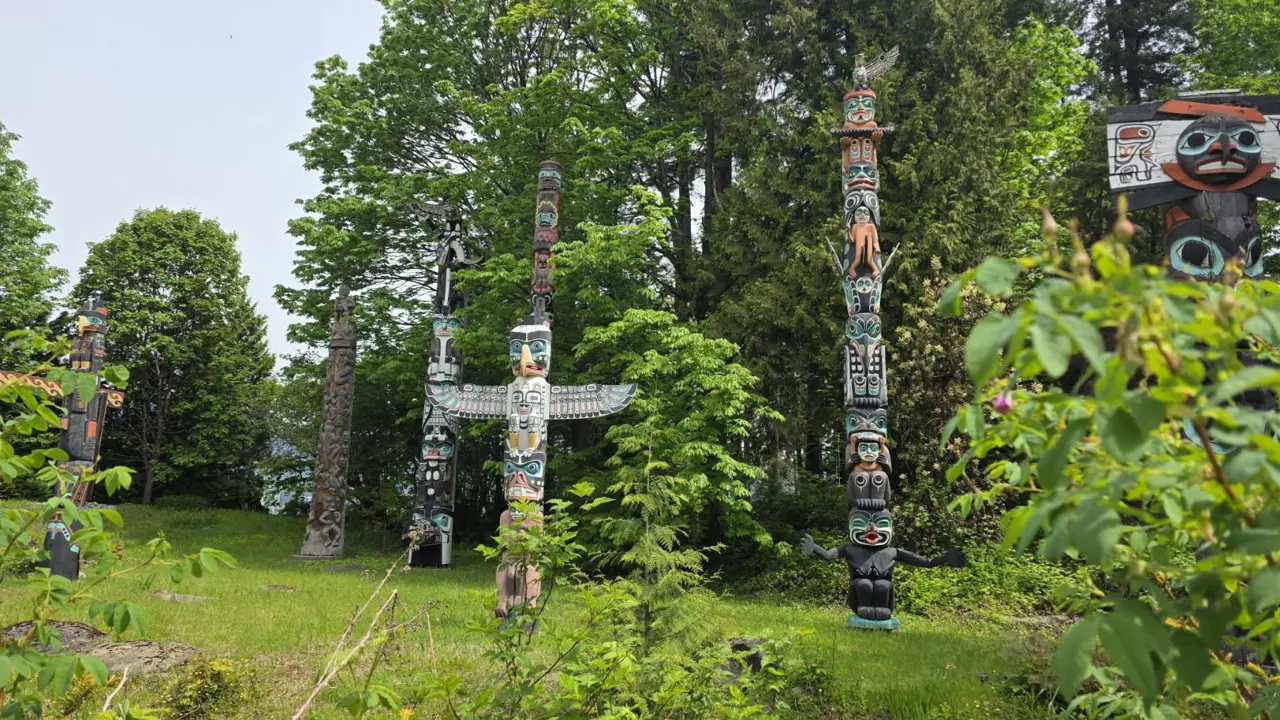 Traditional First Nations totem poles carved from wood, featuring detailed animal and ancestral figures, standing outdoors in Stanley Park in Vancouver