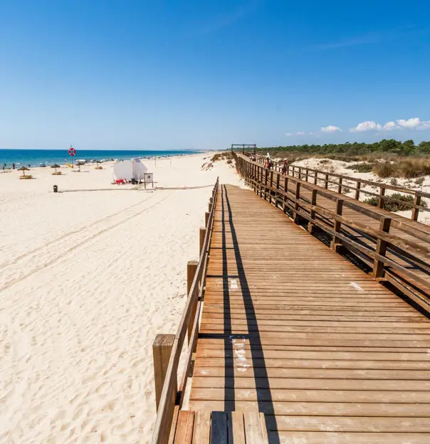 Wooden walkway on the beach at Monte Gordo on the Algarve, with the sandy beach and sea to the left and a shrub area to the right