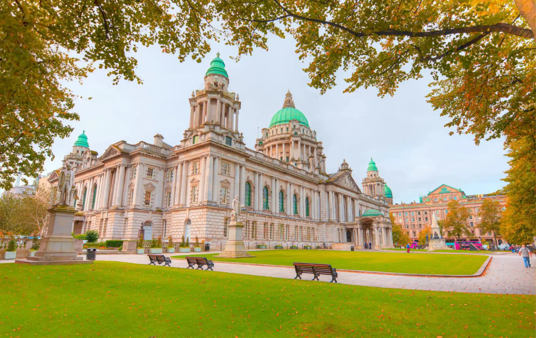 Belfast City Hall, a grand Baroque Revival building with a large central dome and ornate stone façade, on an autumn day surrounded by trees with colourful yellow leaves