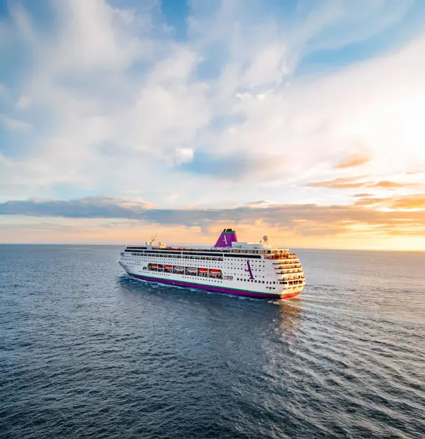 The cruise ship Ambition navigating calm, open waters, with soft sunlight reflecting on the sea