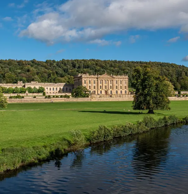 Chatsworth House, an elegant country house beside the River Derwent, with green lawns and wooded hills behind