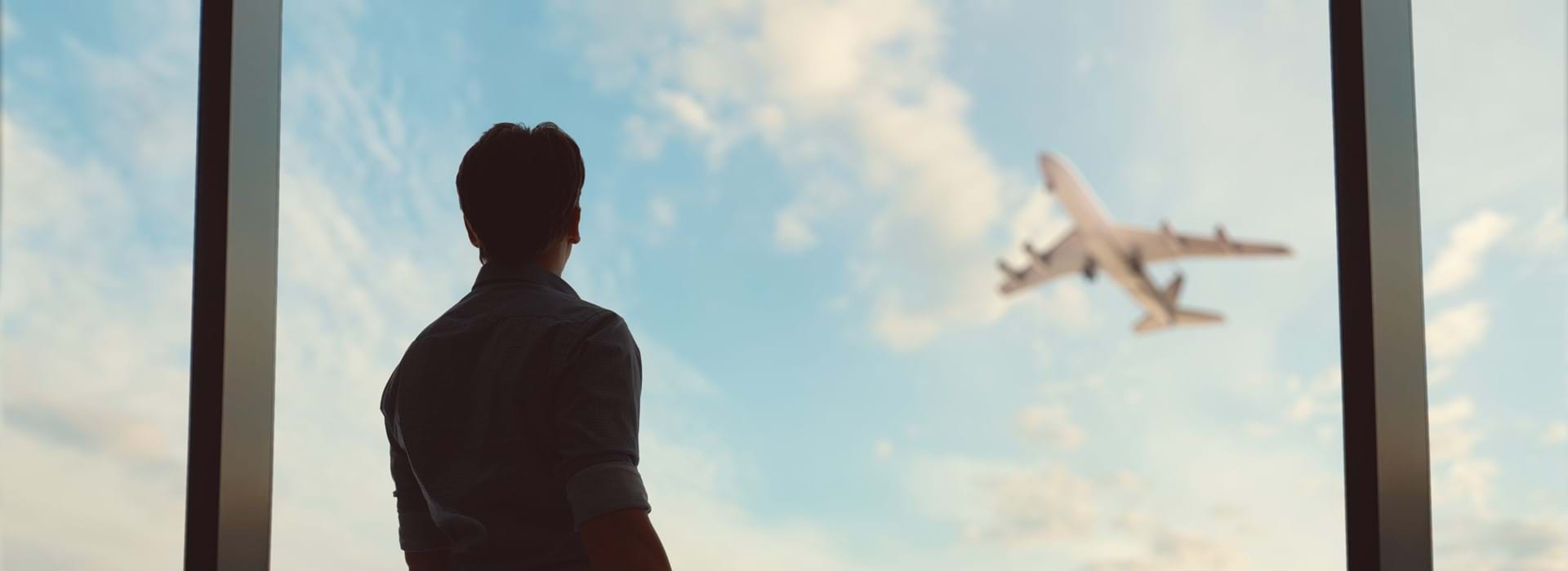 Person looking out the window in an airport at a plane taking off 