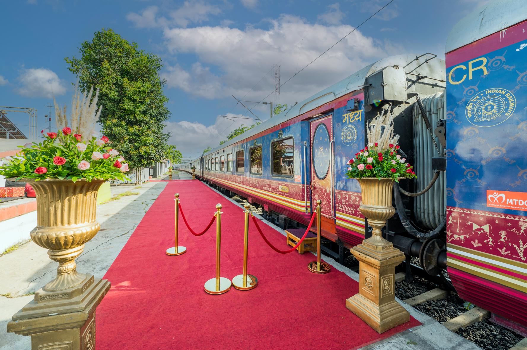Exterior view of the Deccan Odyssey train at the platform, with a red carpet and gold barriers by the entrance