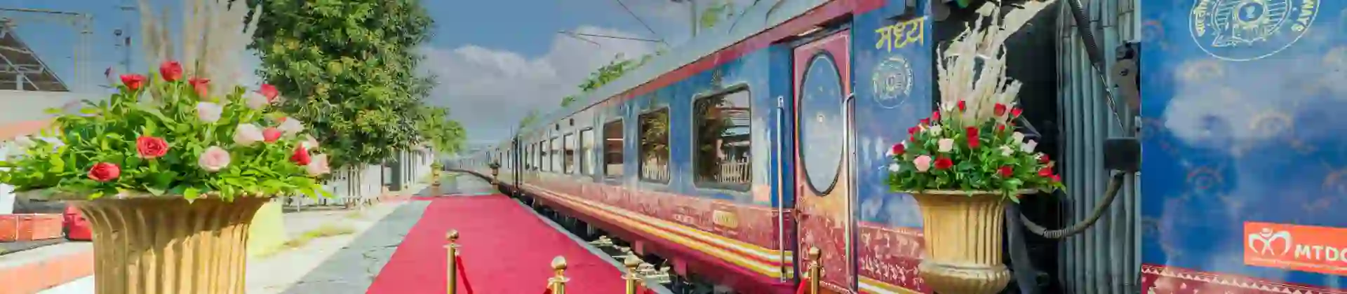 Exterior view of the Deccan Odyssey train at the platform, with a red carpet and gold barriers by the entrance