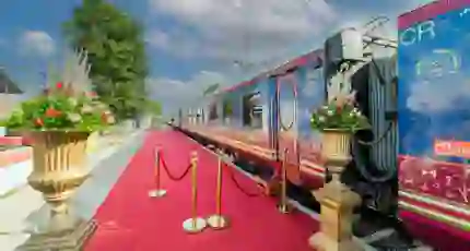 Exterior view of the Deccan Odyssey train at the platform, with a red carpet and gold barriers by the entrance