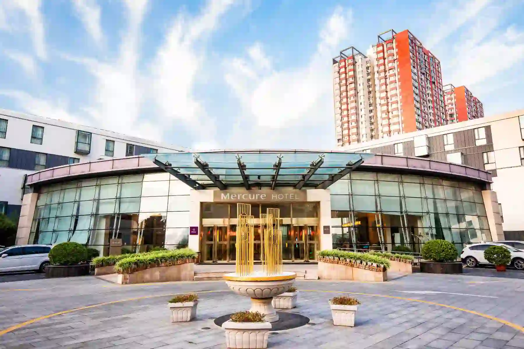 Exterior view of the Mercure Beijing Downtown hotel with a small fountain and potted plants in front of the modern glass entrance in Beijing, China