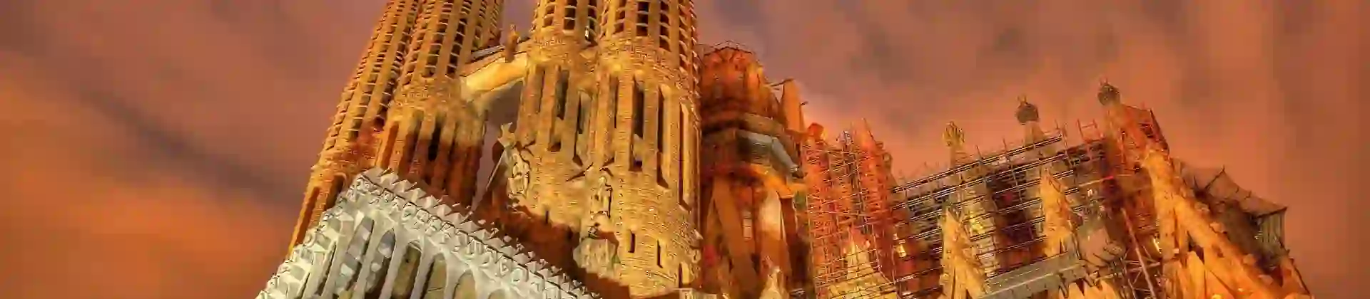 Night view of the illuminated Sagrada Família basilica in Barcelona, Spain, showcasing its intricate architecture and towering spires against a dramatic, cloudy sky