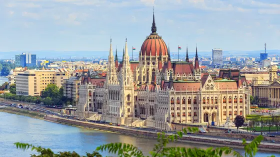 High angle shot of Hungarian Parliament Building, with red roofs and spiky turrets. Danube river in the left forefront