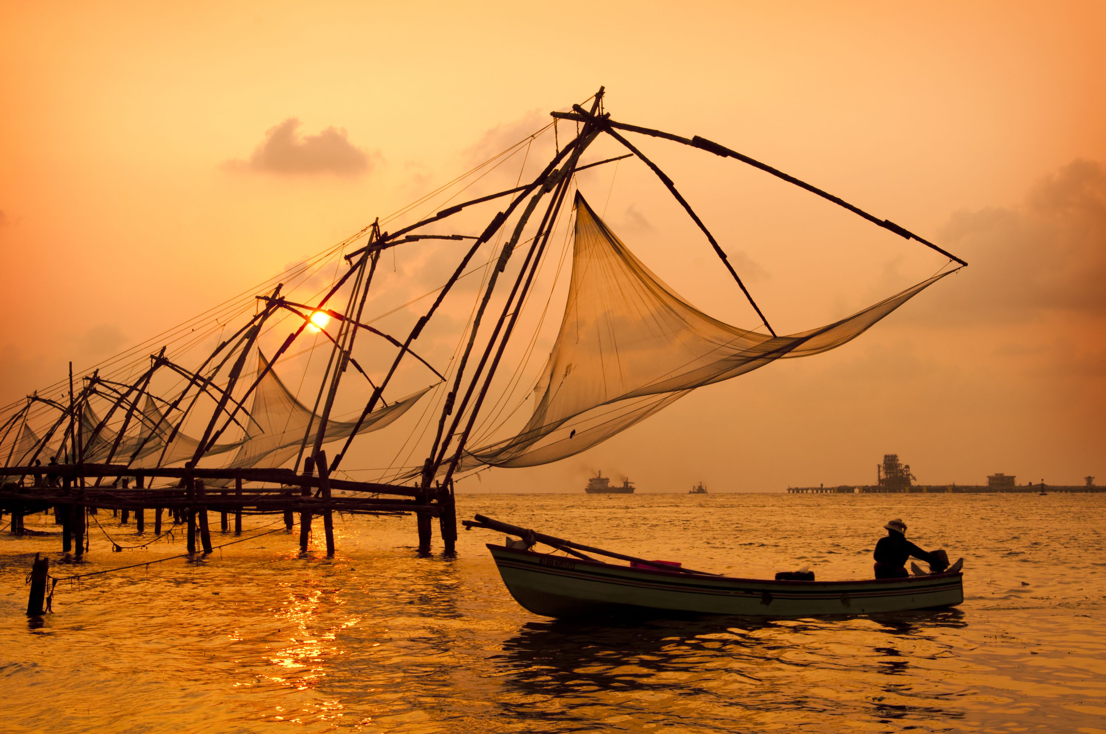 Chinese fishing nets at sunset in Kochi, India, silhouetted against the glowing sky and calm water